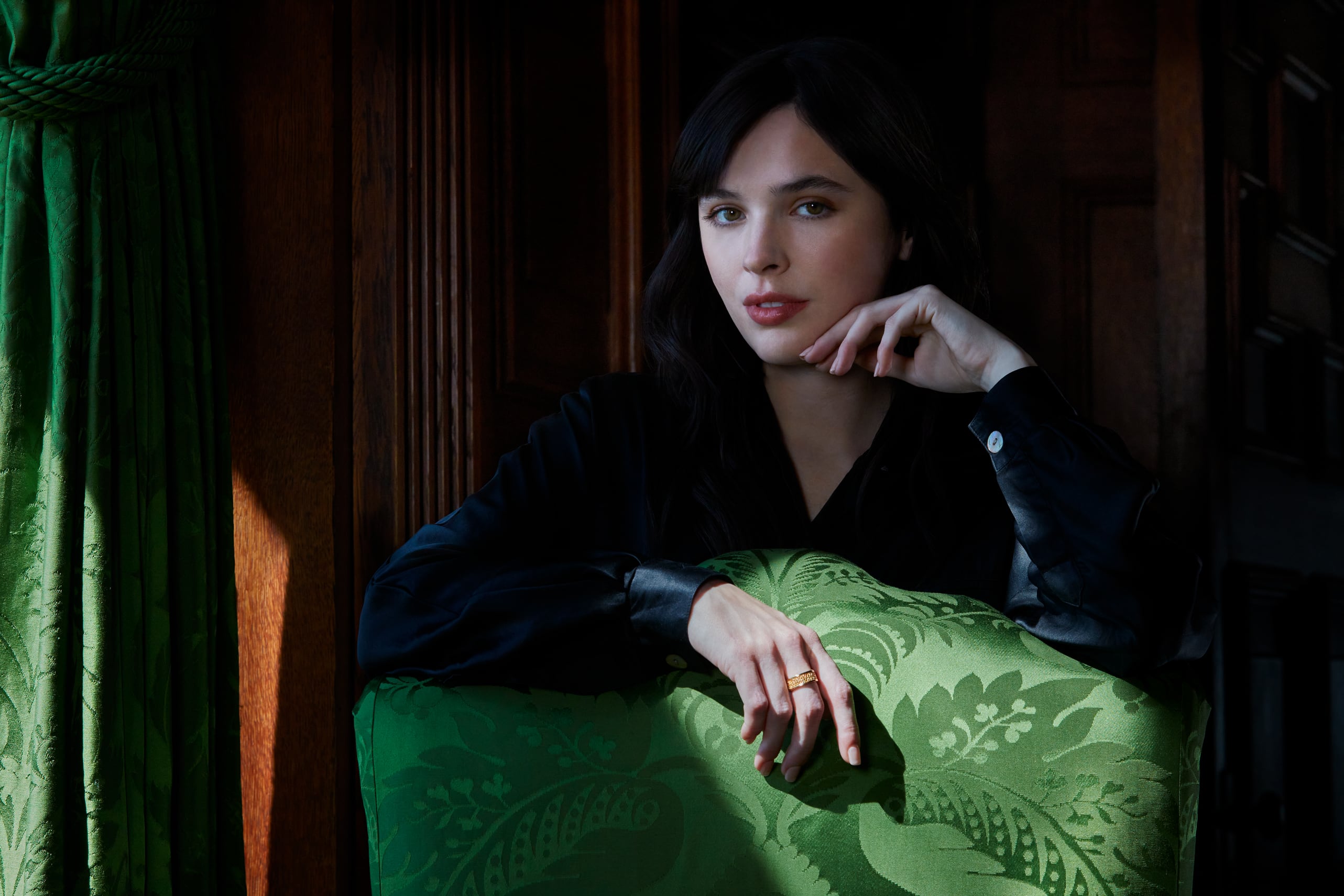 A woman stands behind a green chair in the Oak Sitting Room, wearing an Oak Sitting ring