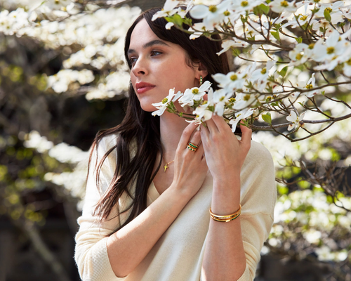 A woman stands among dogwood trees, earing jewelery from Avermore's Stuyvesant collection