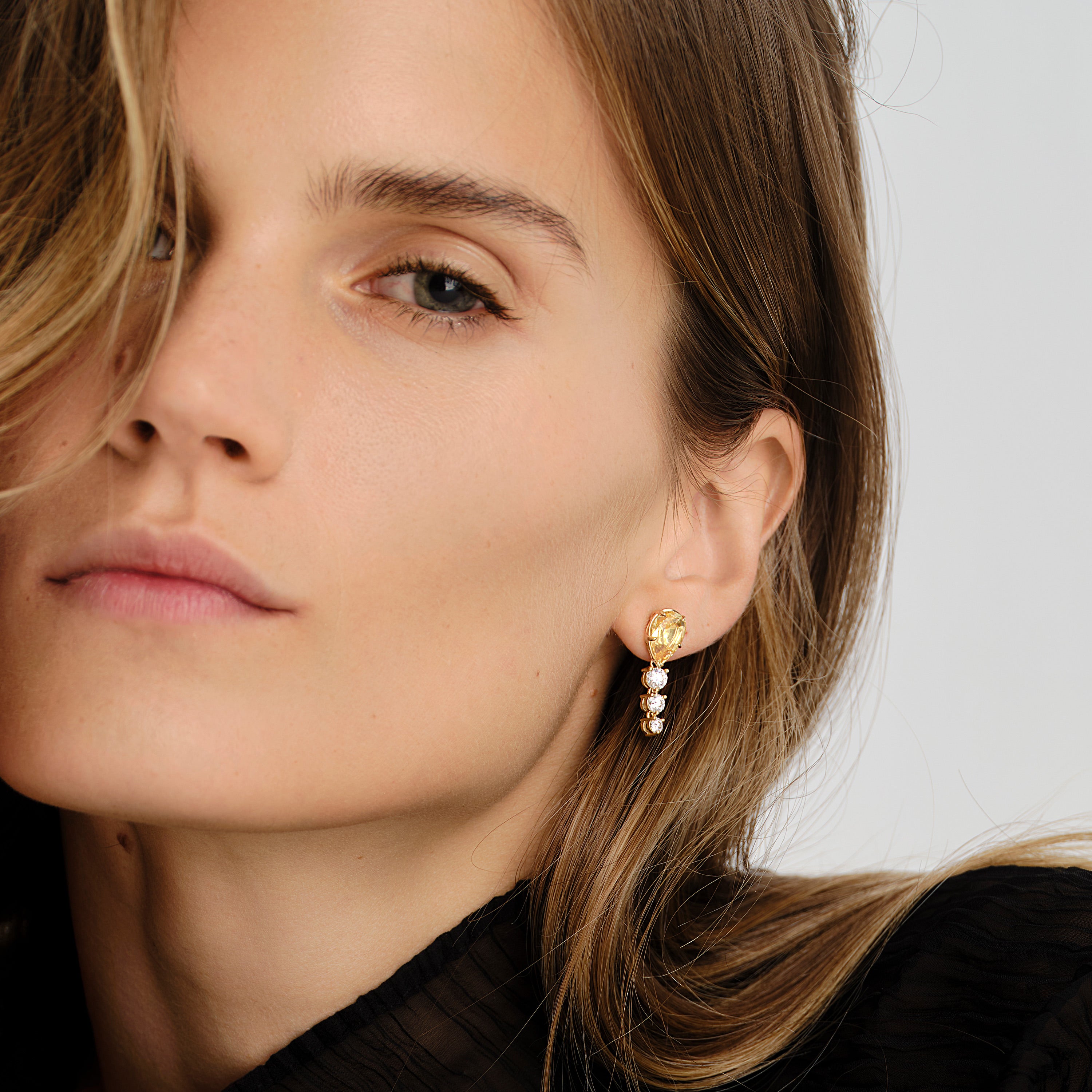 Close-up of a woman wearing gold and sapphire earrings against a neutral background