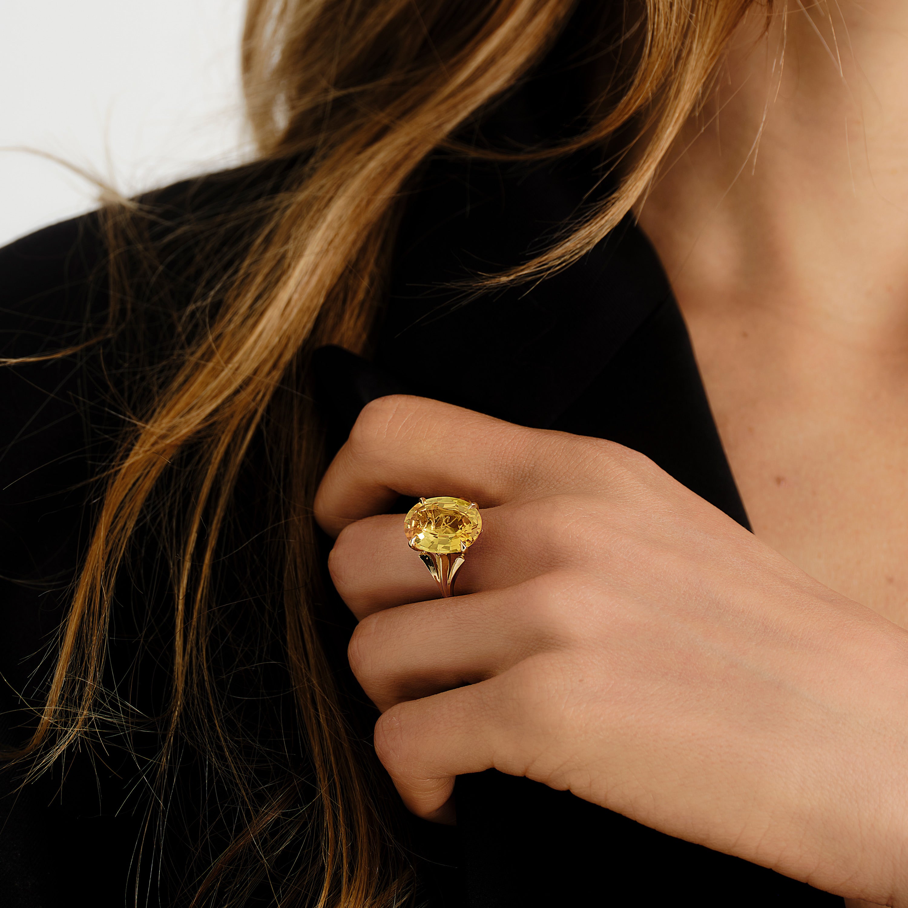 Close-up of a hand wearing a gold ring with a yellow sapphire 