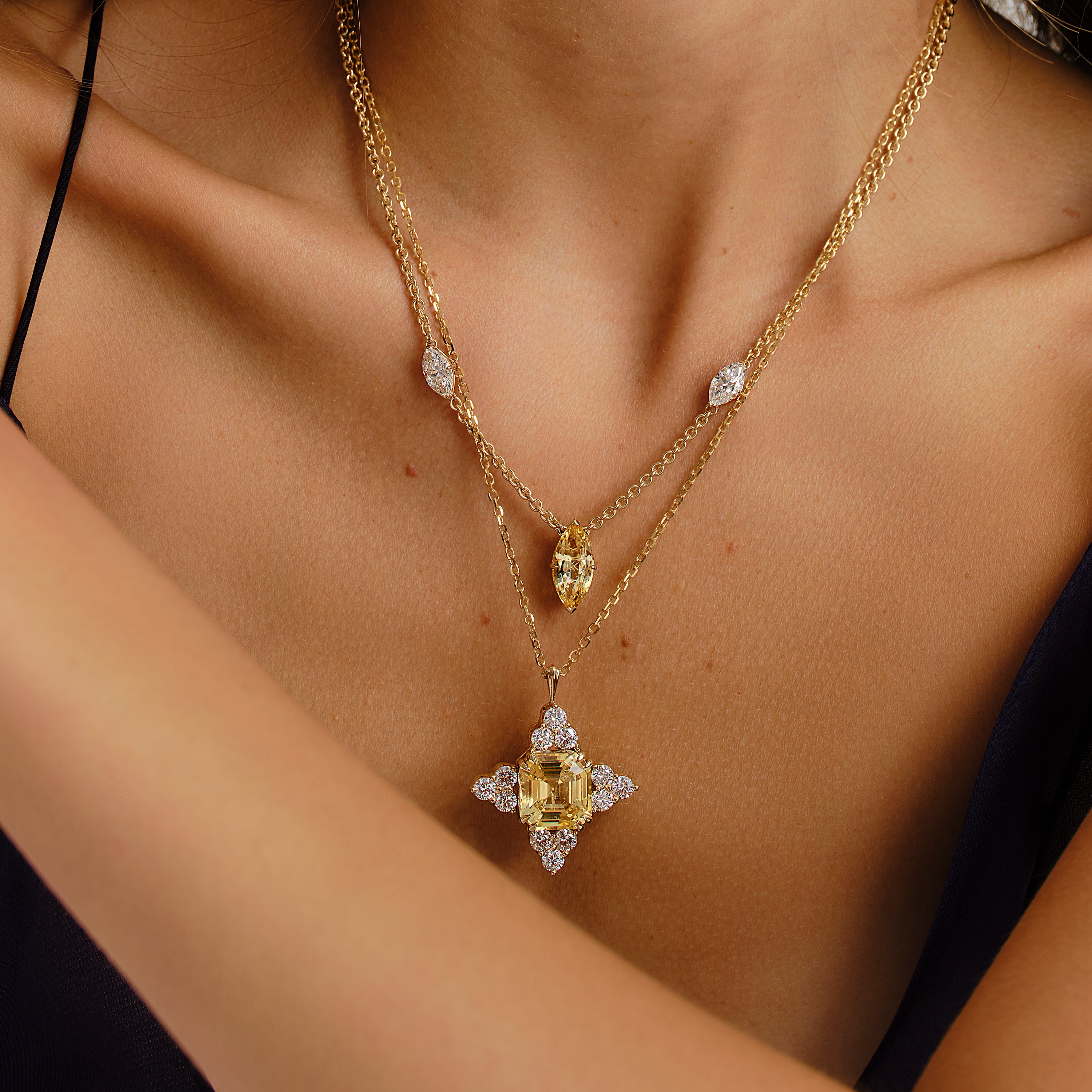 Gold necklace with a yellow sapphire and diamond brooch on a person wearing a black dress.