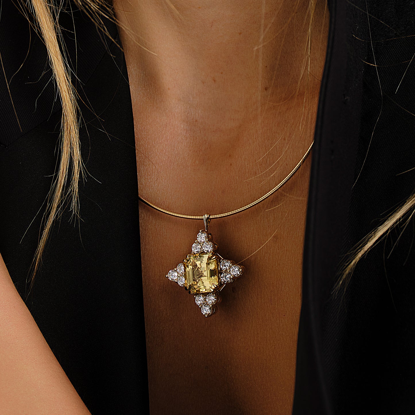 Gold necklace with a yellow sapphire and diamond brooch on a person wearing a black dress.
