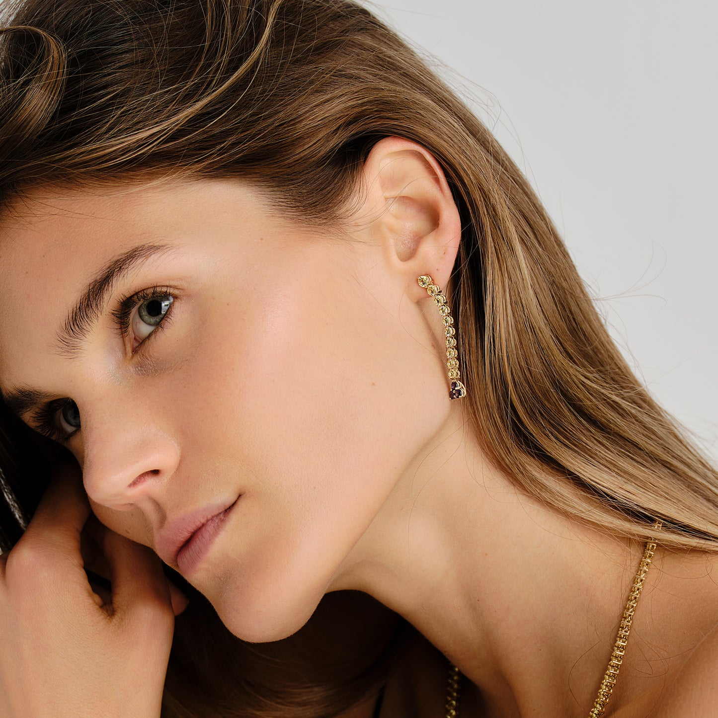 Close-up of a woman wearing gold earrings with yellow sapphires and a purple sapphire drop 