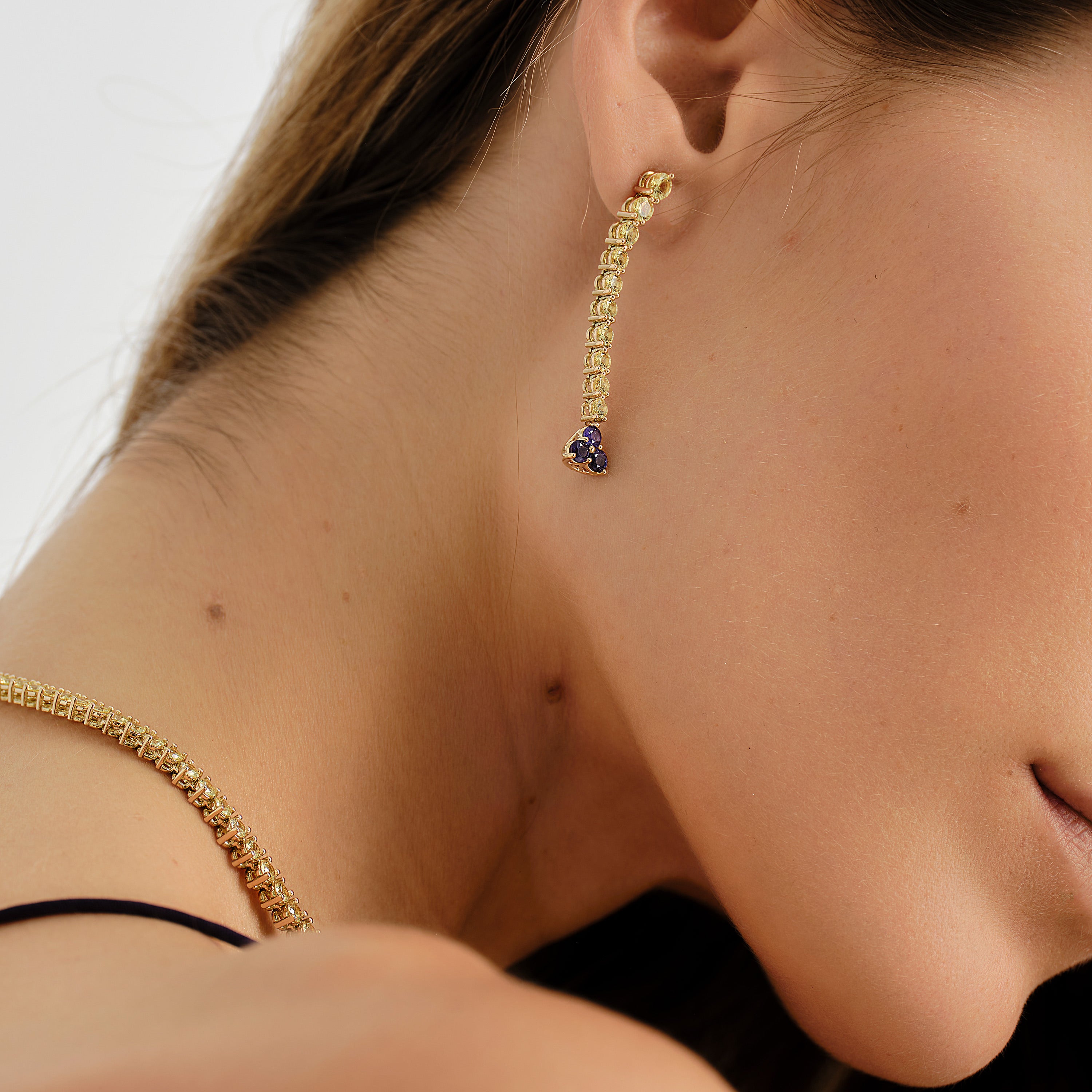 Close-up of a woman wearing gold earrings with yellow sapphires and a purple sapphire drop 