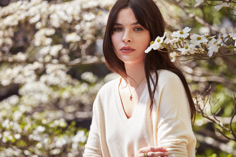 A woman surrounded by flowers, wearing an Heirloom cross necklace